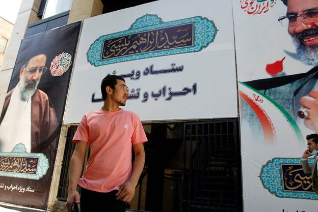 A man stands in front of large poster for Ebrahim Raisi, the conservative frontrunner in Iran's election. 